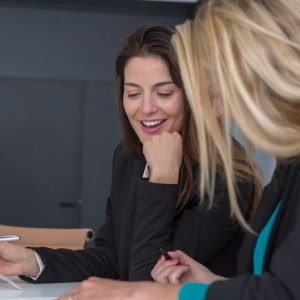 Two professional women discussing documents at an office meeting, showcasing teamwork and partnership.